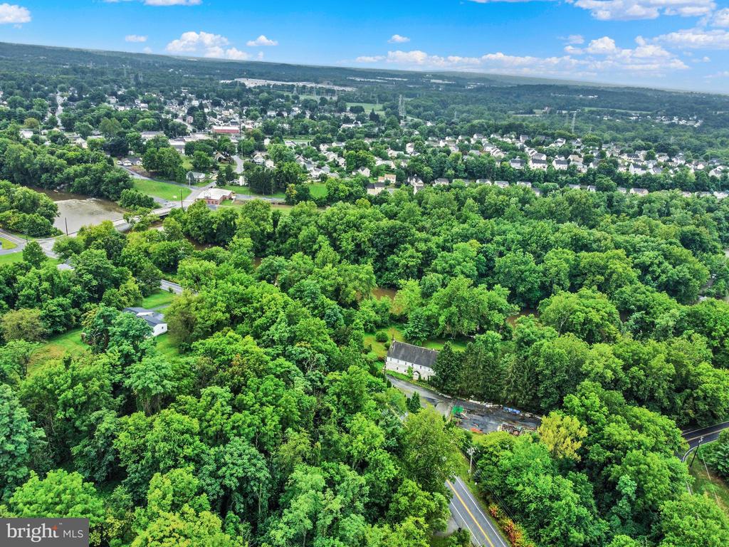 Aerial view of wooded property with a creek, road, and town in the distance.
