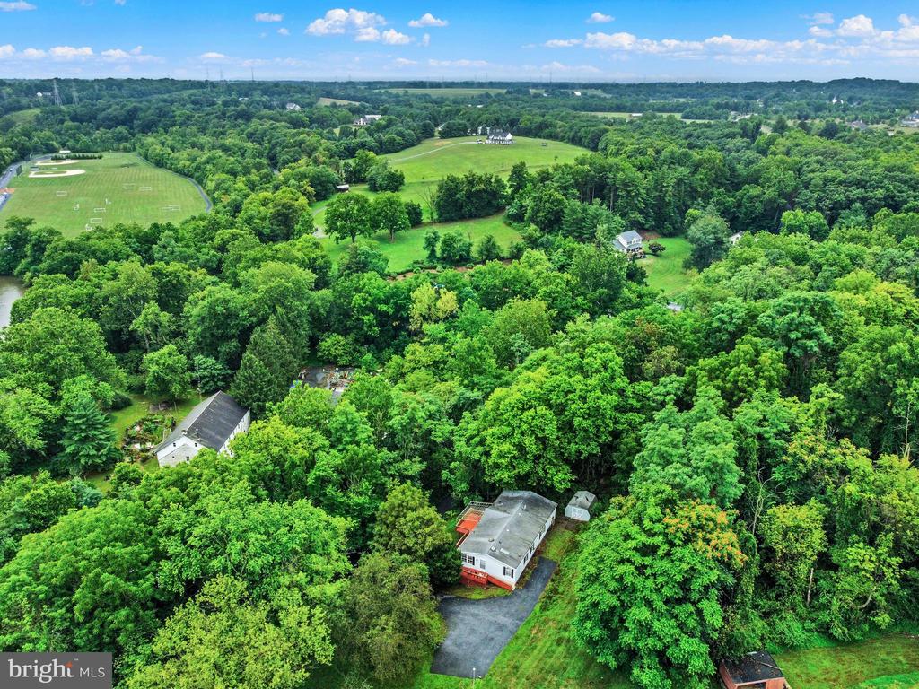 Aerial view of a home among dense trees, with open fields and sports fields beyond.