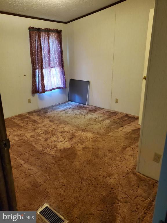 Empty bedroom with patterned brown carpet, a curtained window, and a screen leaning against the wall.