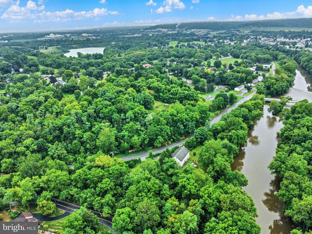 Aerial view of wooded property beside a river, with a road and homes nearby.