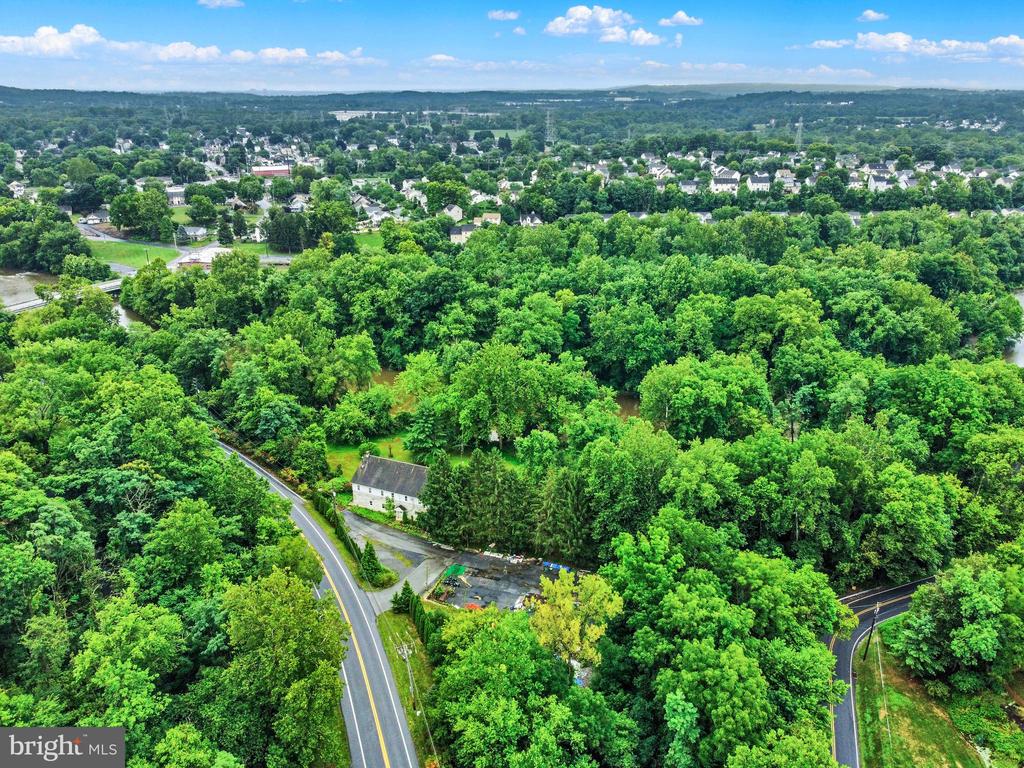 Aerial view of a house nestled among dense trees, with curving roads and a distant neighborhood.