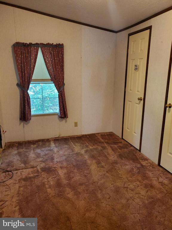 Vacant room with brown patterned carpet, red window curtains, and two doors.