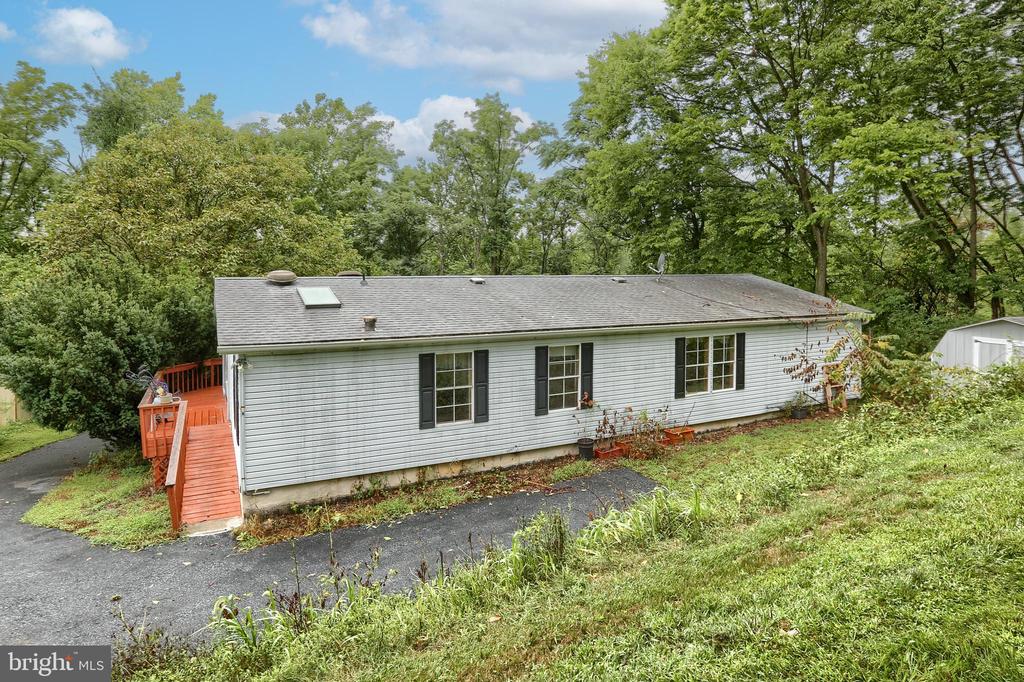 Single-story home among mature trees, with a red-orange deck and paved driveway.