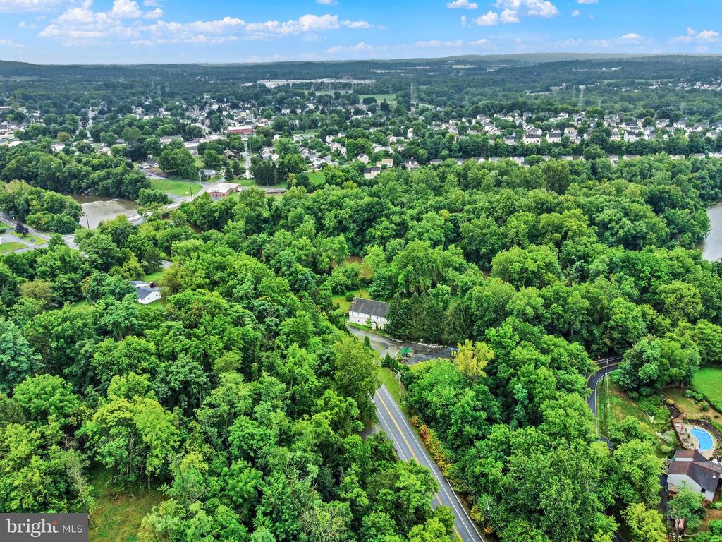 Aerial view of a wooded property with a house and road, with a town and river beyond.