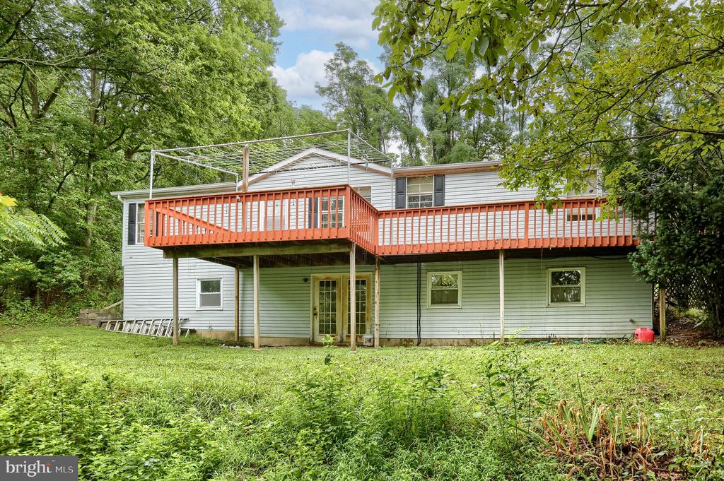 Rear of a light-colored house with a long elevated orange-red deck, surrounded by trees and a grassy yard.