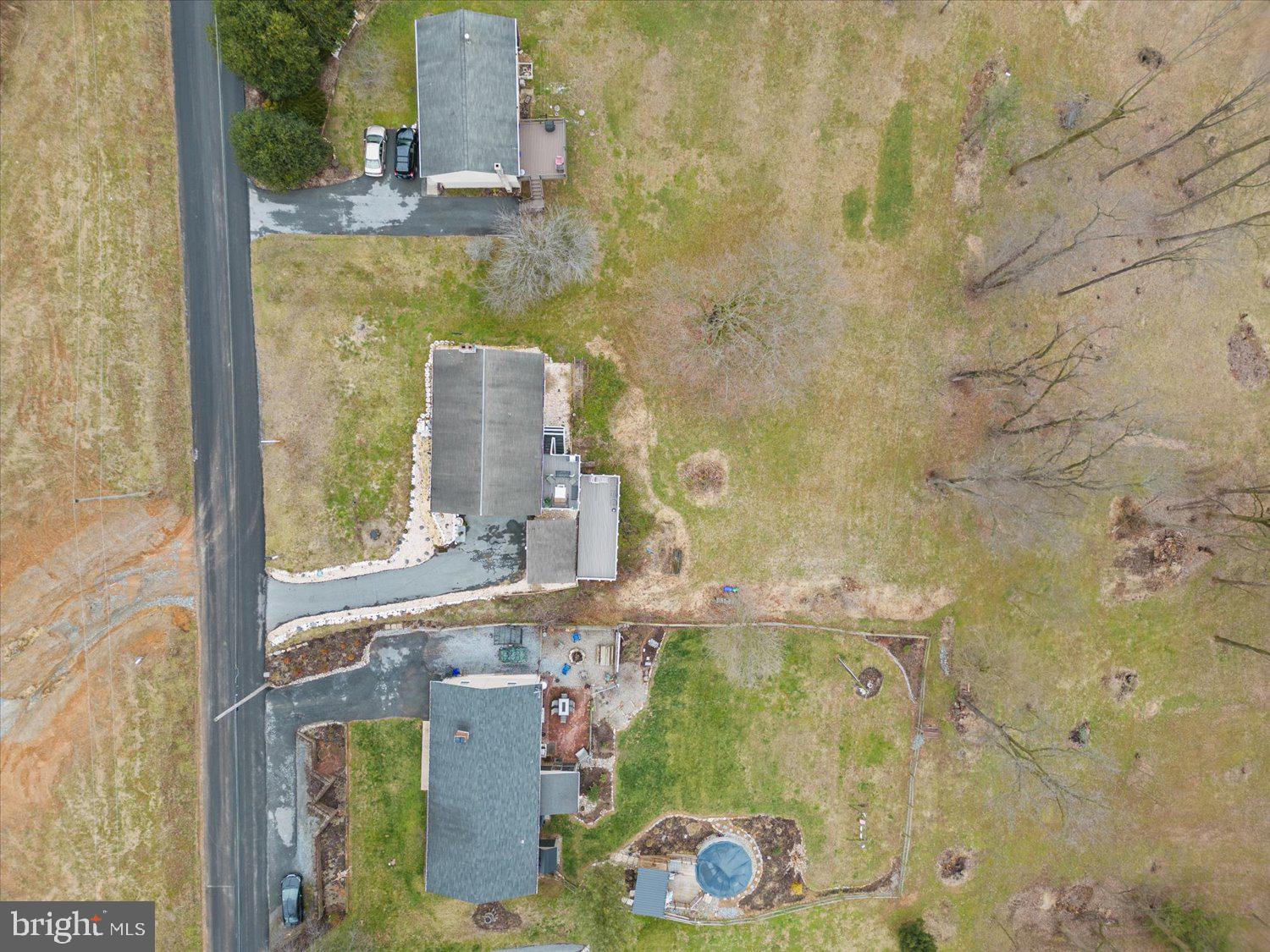 Aerial view of homes with broad grassy yards, leafless trees, and a backyard swimming pool.