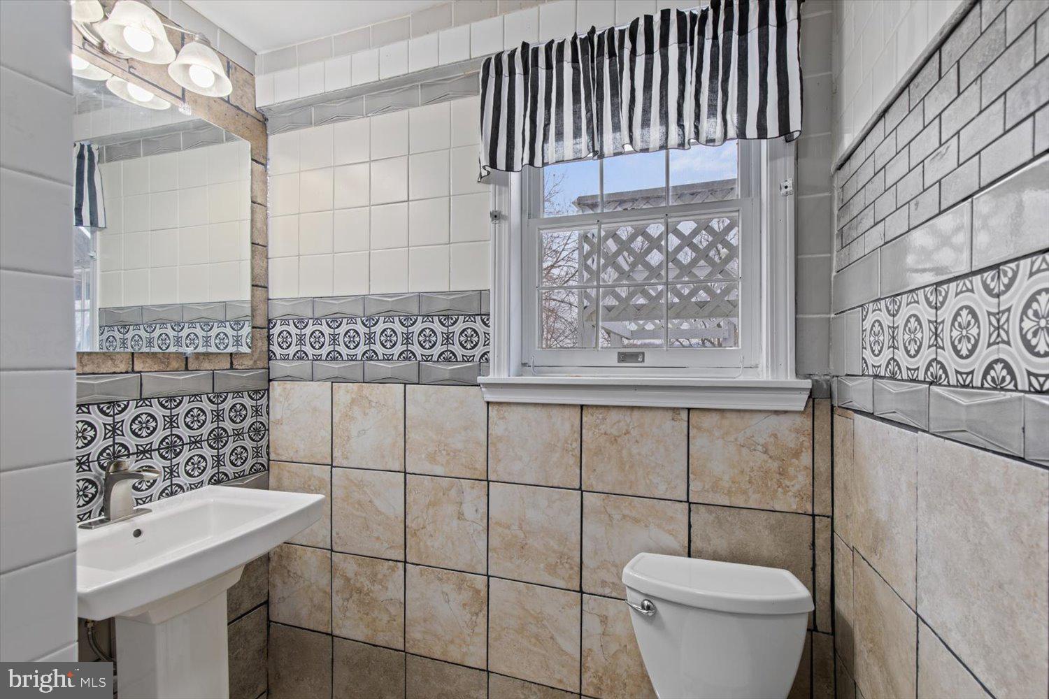 Bathroom with patterned tile, a white sink and toilet, and a window with a striped valance.