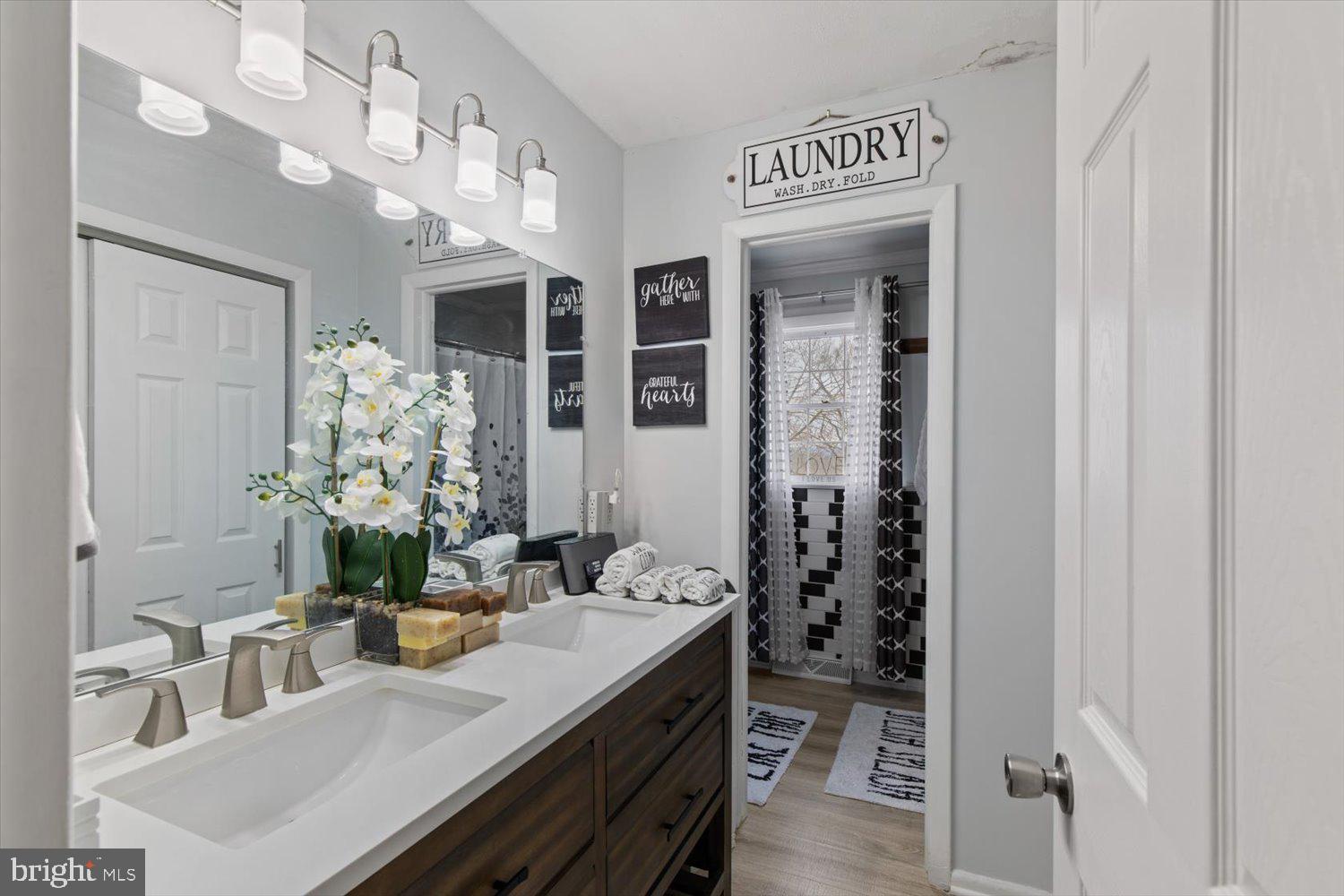 Bathroom with a dark wood double vanity, white countertop, orchid, and doorway to a black-and-white tiled shower.
