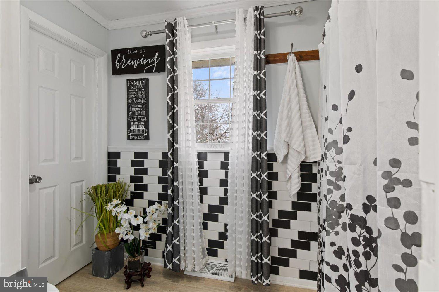 Bathroom with black-and-white subway tile, a window, patterned curtains, and white towels.