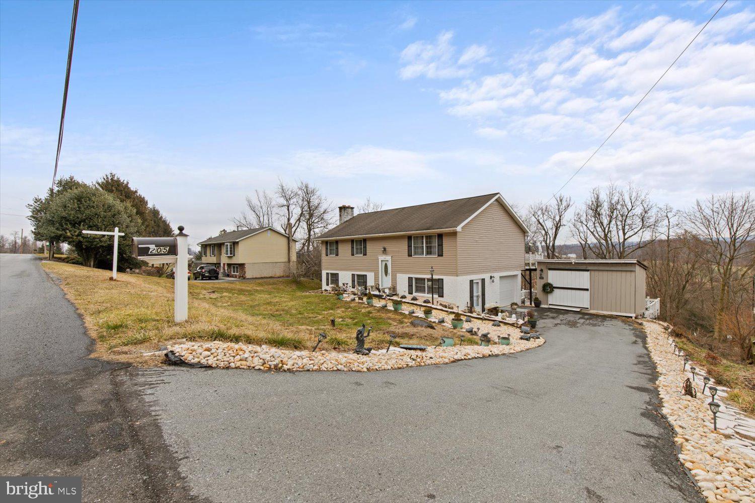 Tan split-level home with an attached garage, detached outbuilding, and curved driveway.