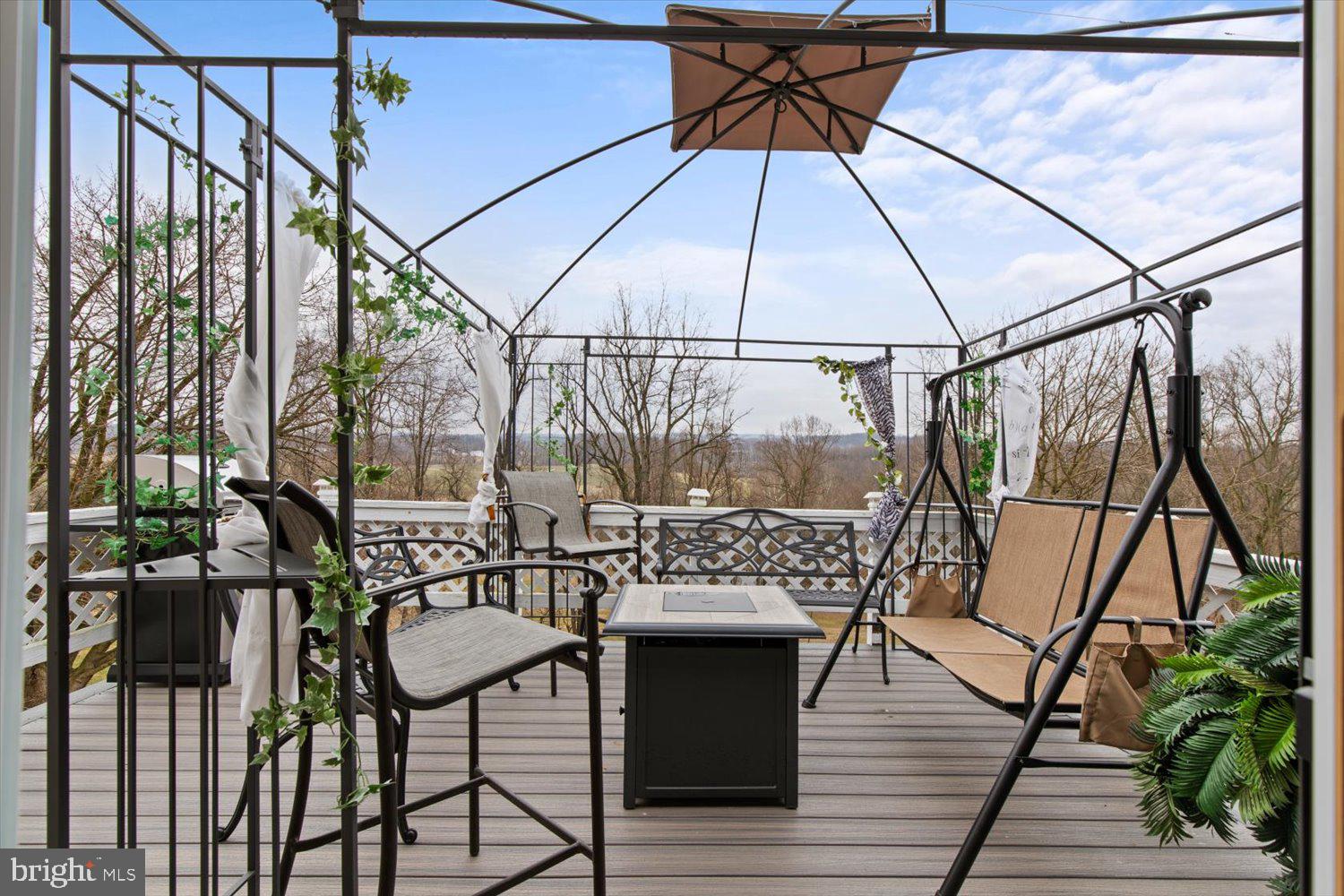 Furnished deck beneath a canopy frame, with patio seating and a wooded view.