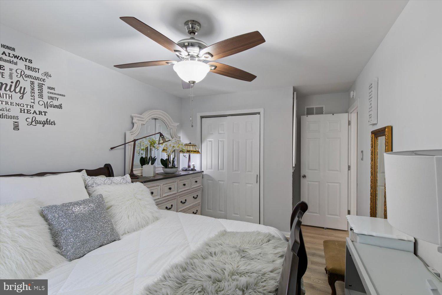 Bedroom with a white bed, fluffy pillows, an ornate dresser, and a wood-blade ceiling fan.