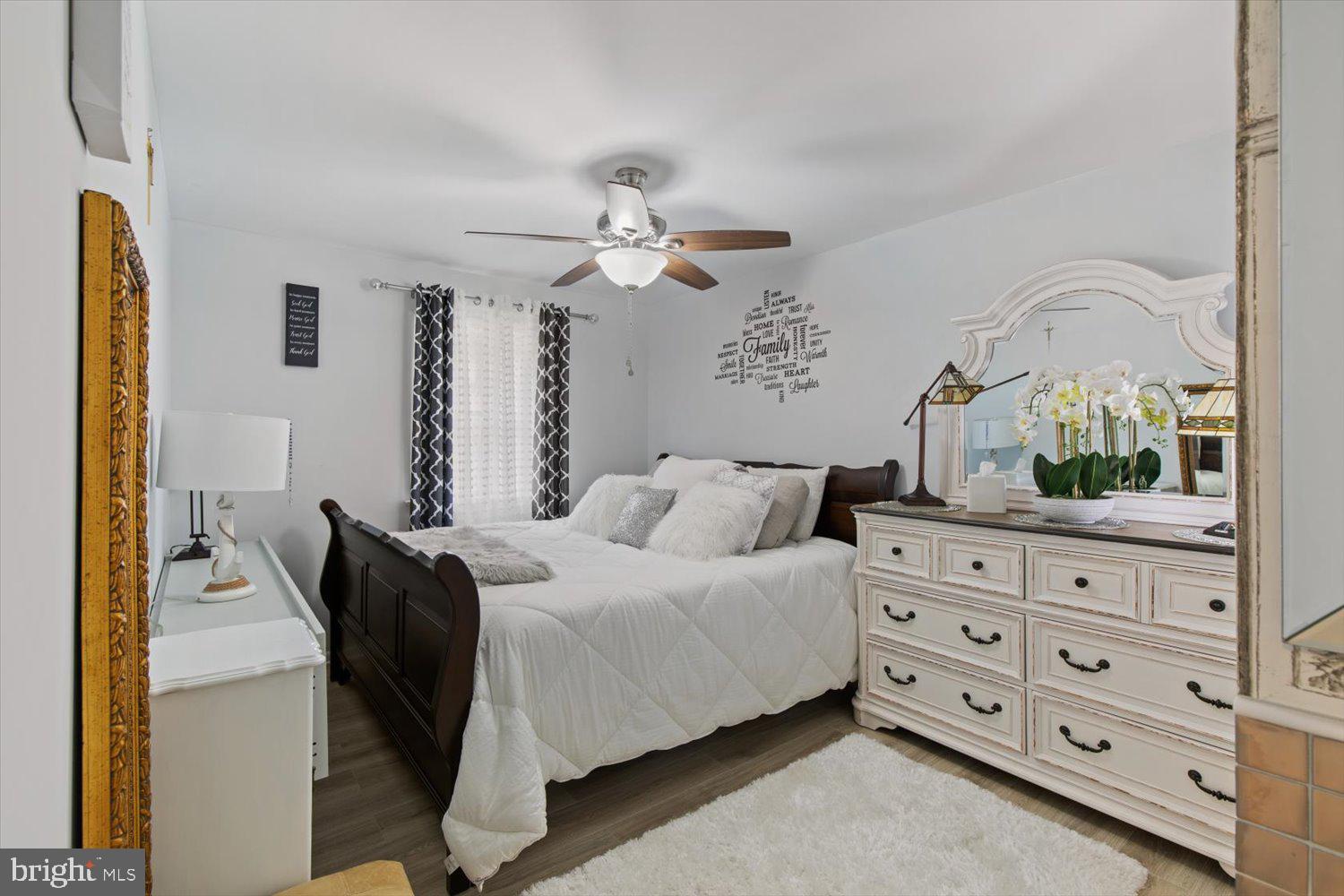Bedroom with a dark wood bed, white bedding, and ornate white dresser and mirror.