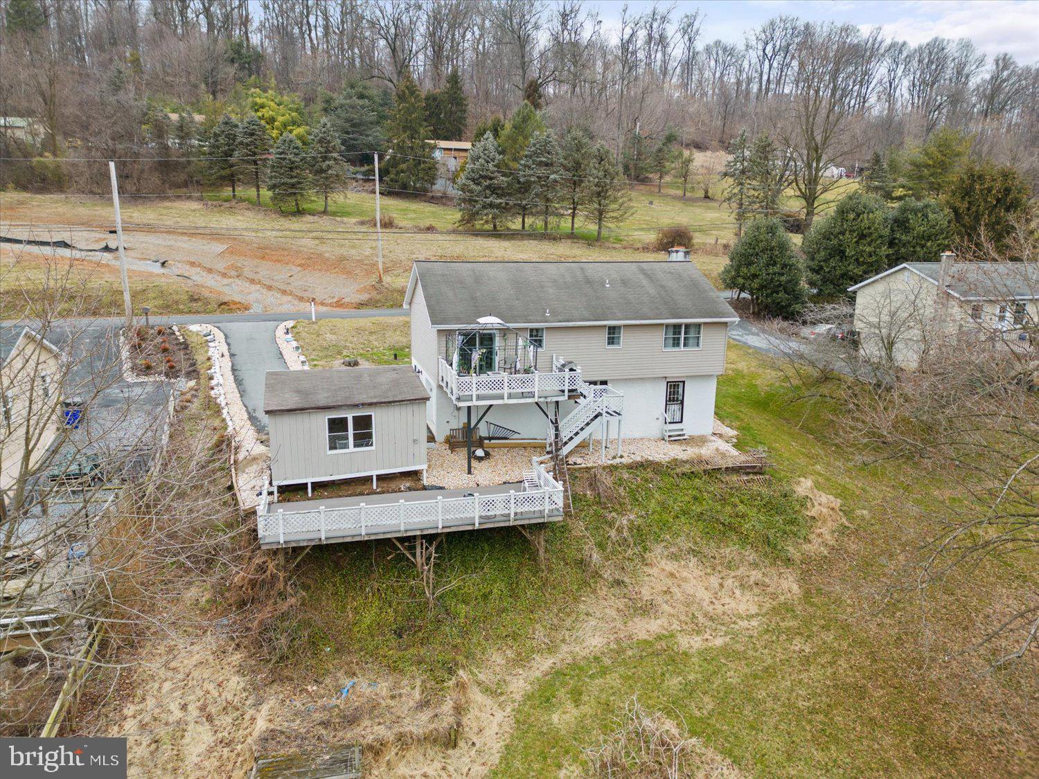 Aerial view of a raised home with a large deck, exterior stairs, and a spacious wooded yard.