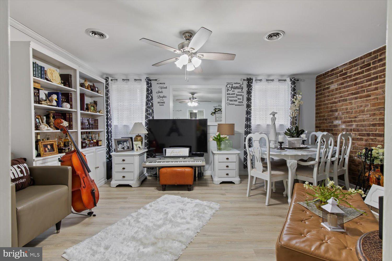 Furnished living and dining room with built-in shelves, exposed brick wall, piano, and cello.
