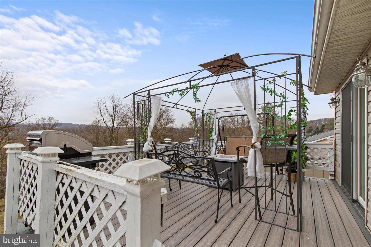 Furnished raised deck with a vine-covered pergola, patio seating, grill, and wooded hillside views.