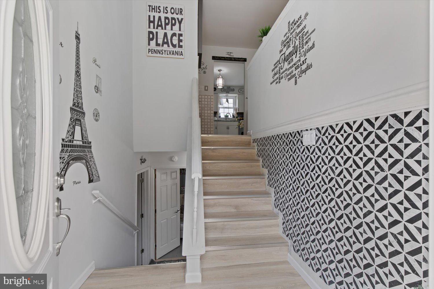 Entryway staircase with geometric wallpaper, an Eiffel Tower decal, and a view toward the kitchen.