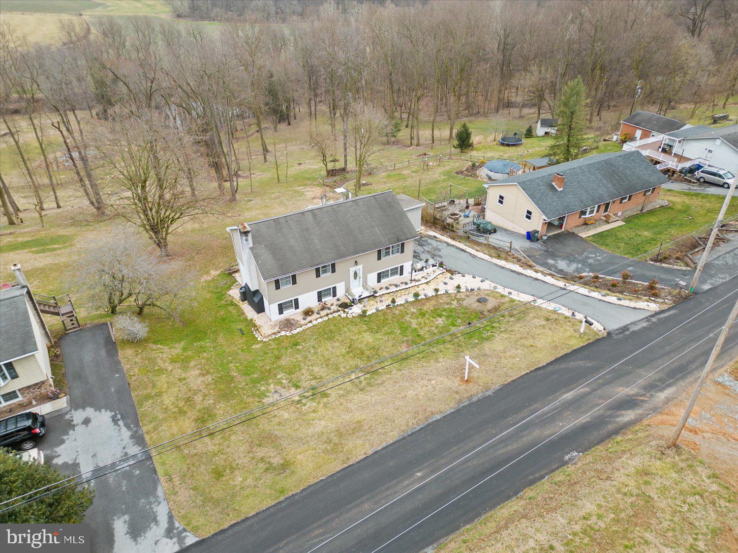 Aerial view of a detached house with a broad yard and woods behind it.