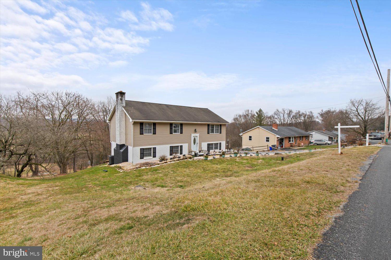 Split-level home with tan siding and white lower level on a sloping lawn.