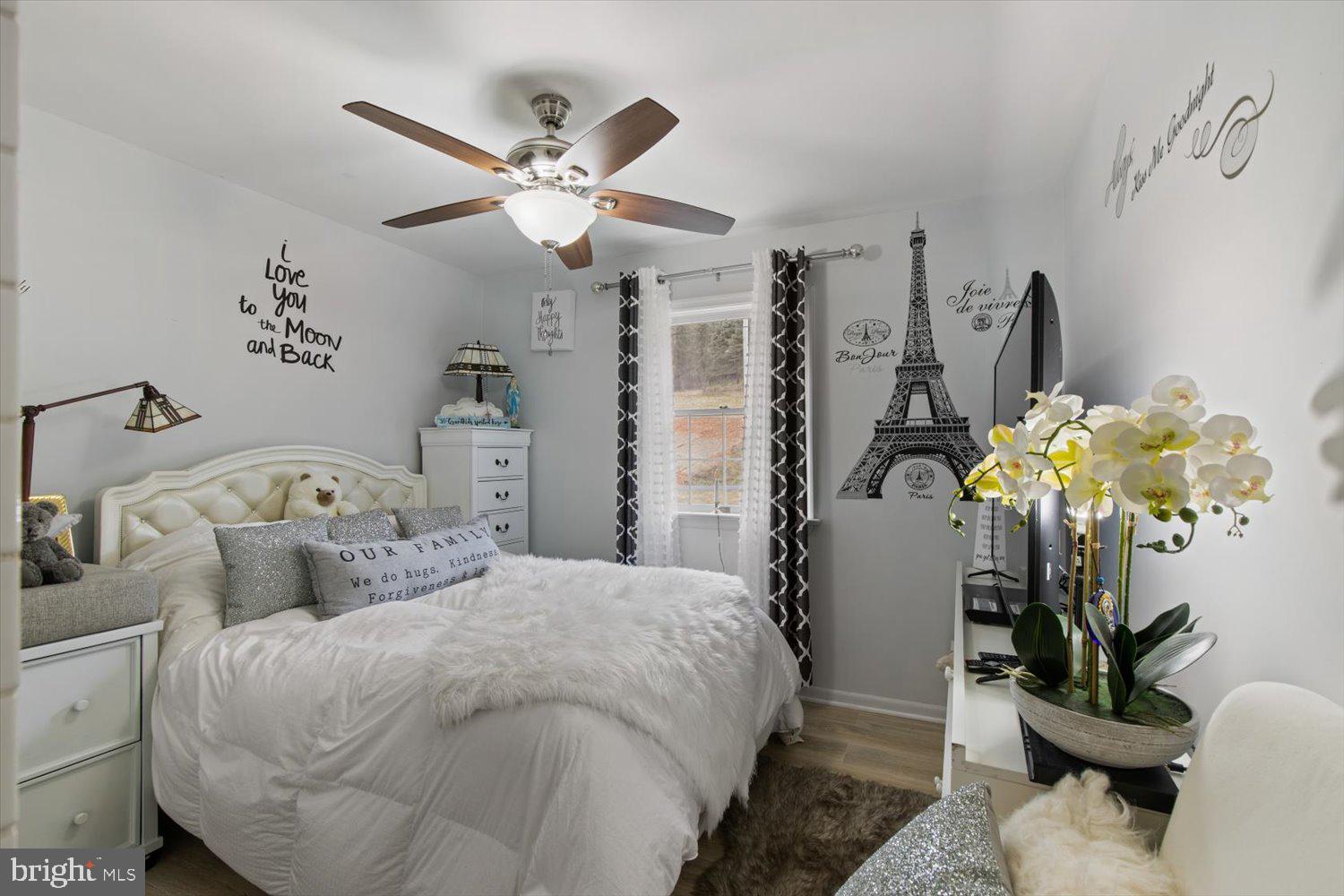 Bedroom with a white bed, tufted headboard, ceiling fan, and Eiffel Tower wall art.