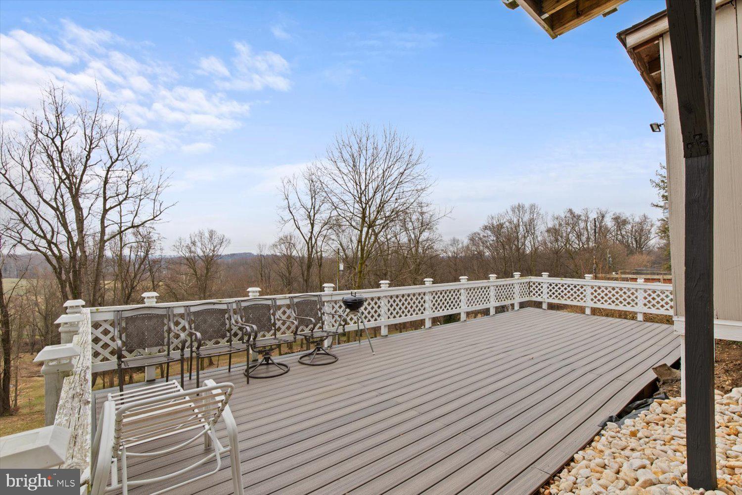 Spacious deck with white lattice railings, patio chairs, and a wooded view.
