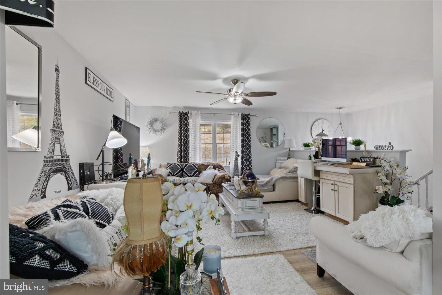Living room and home office with white furnishings, patterned cushions, and Eiffel Tower wall art.