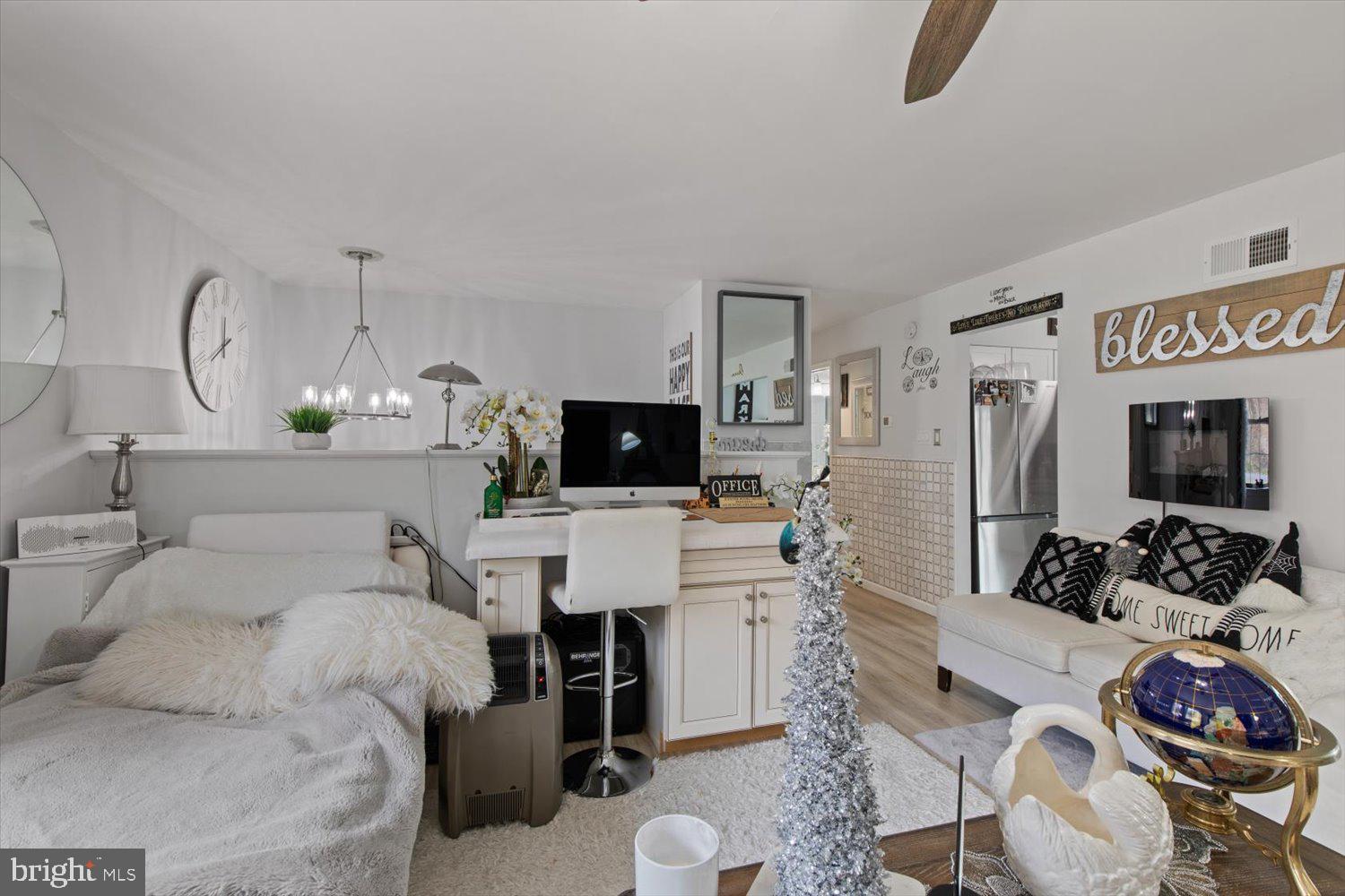 Furnished bedroom with a bed, office desk, white sofa, and stainless-steel refrigerator.