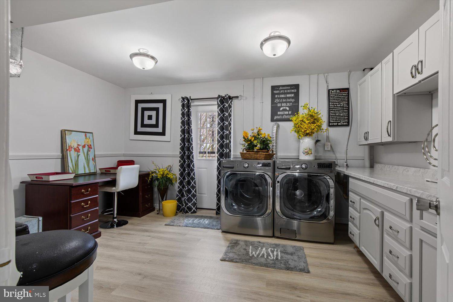 Laundry room with front-loading washer and dryer, white cabinetry, and a desk beside the door.