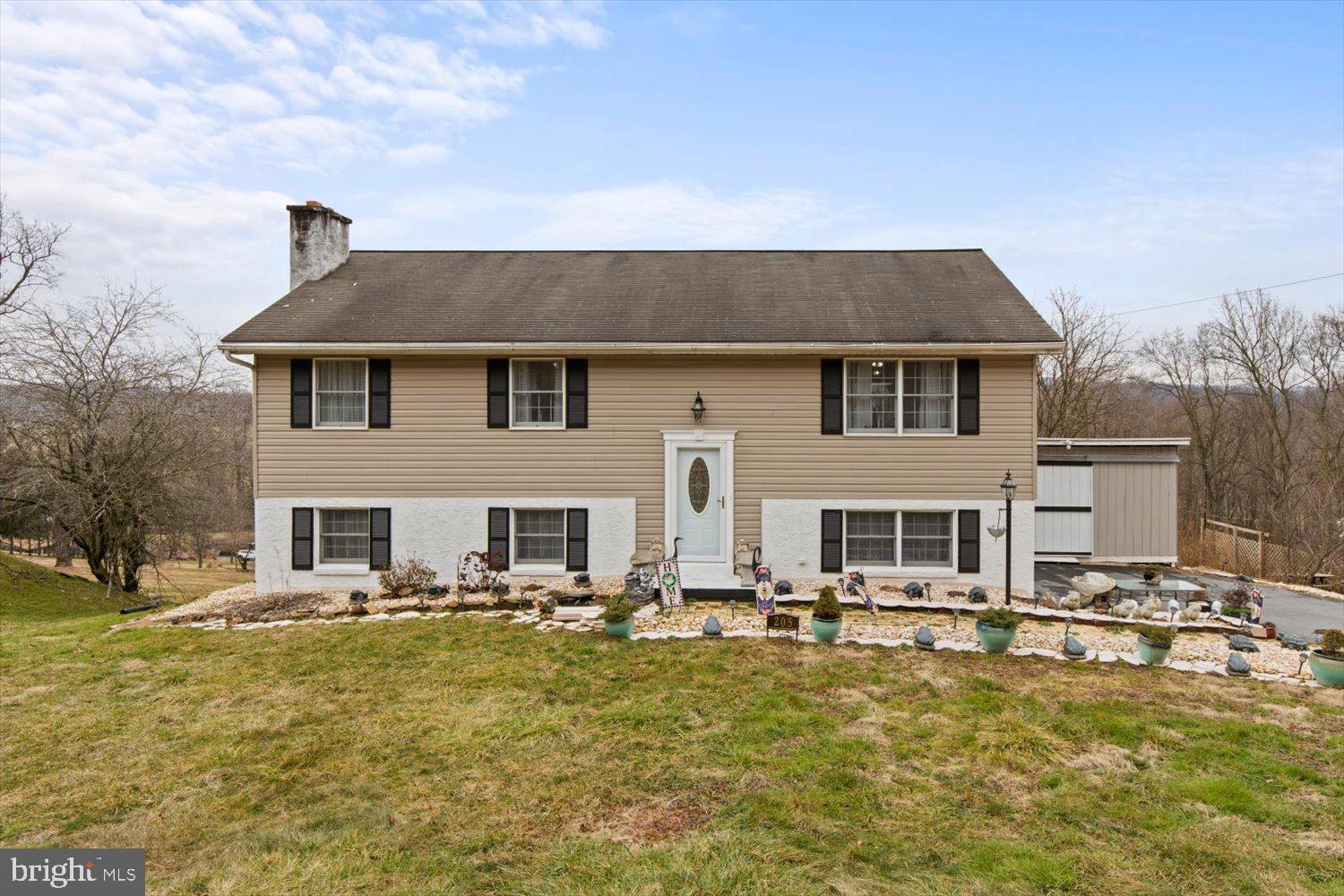 Beige split-level house with dark shutters, white front door, and stone-edged garden beds.