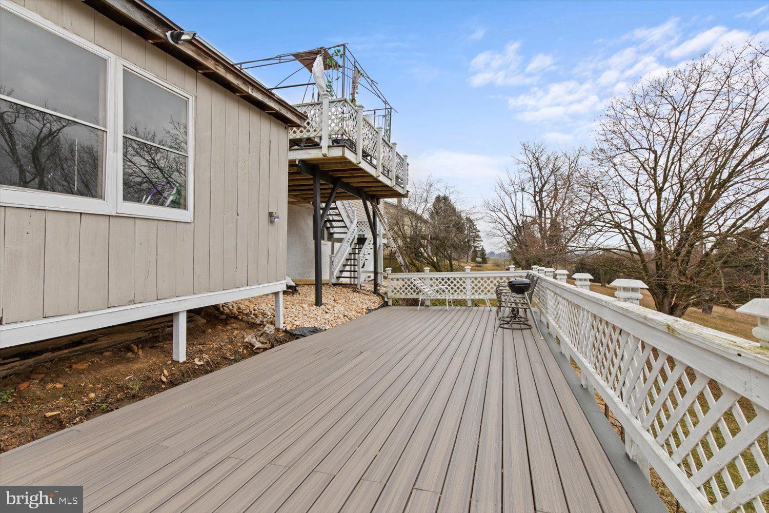 Broad gray deck with white lattice railings, an upper deck, stairs, and a barbecue grill.
