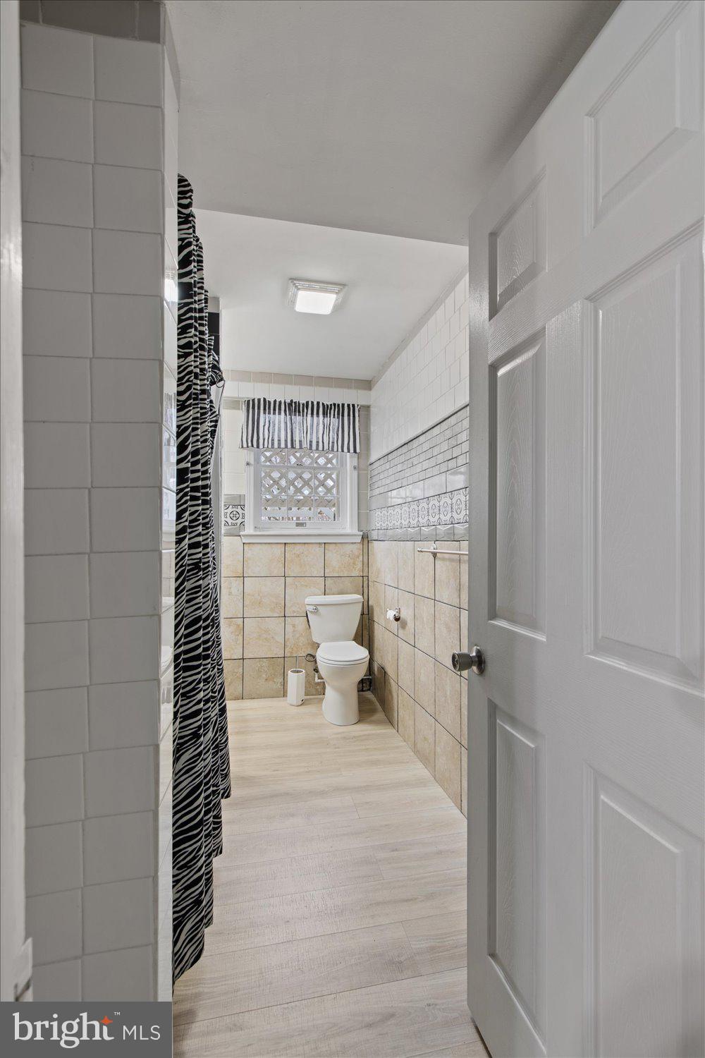 Bathroom with beige tile, a toilet beneath a small window, and a black-and-white striped shower curtain.