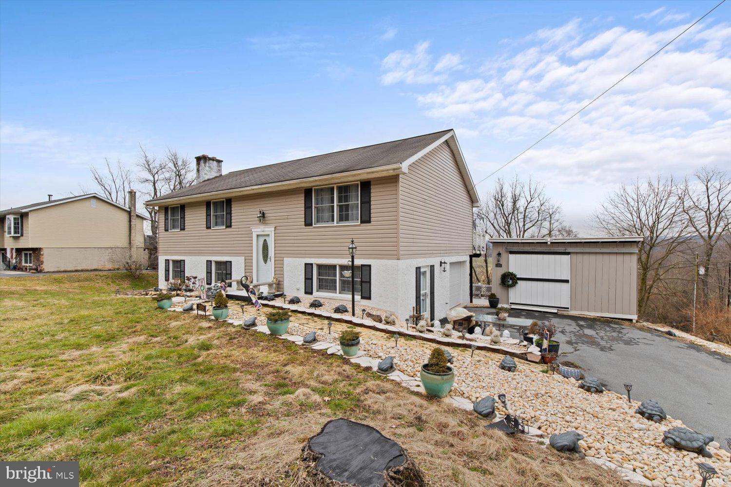 Beige split-level home with black shutters, stone landscaping, and a detached garage.