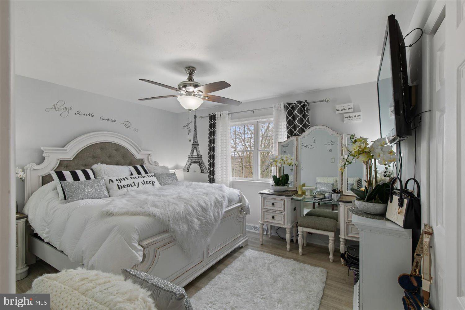 Bedroom with an ornate white bed, vanity, mirrored dresser, and large window.