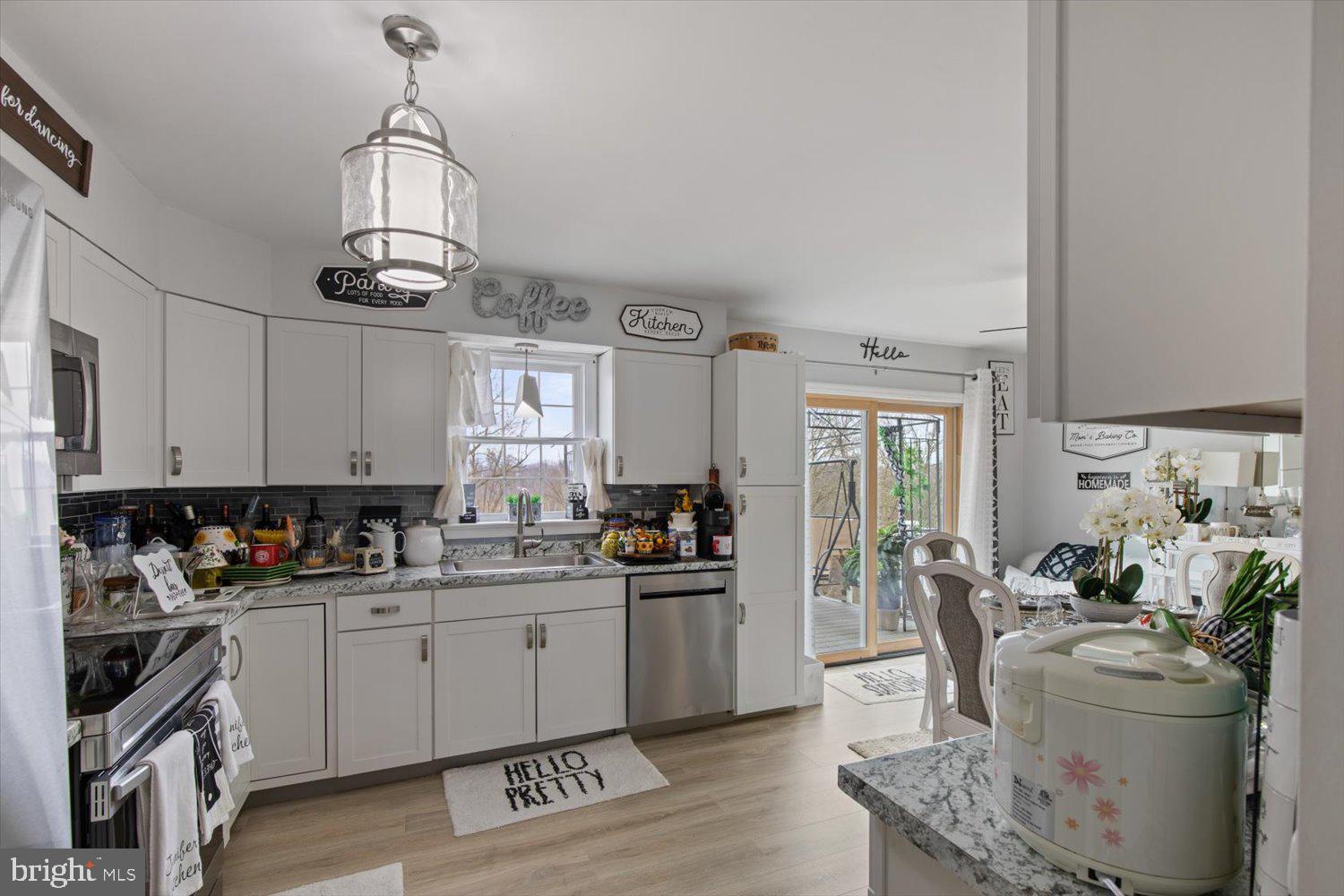 Bright white kitchen with gray countertops, dark tile backsplash, and sliding glass doors beside the dining area.