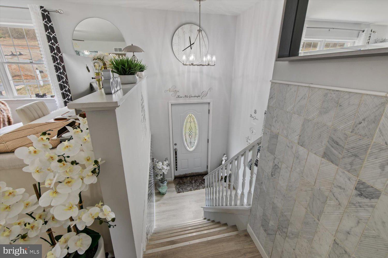 Decorated staircase descends to a white front door, with geometric gray tile and orchids in the foreground.