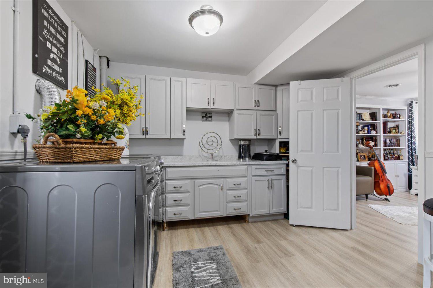 Laundry room with white cabinetry, a washer and dryer, and an open doorway to a room with a cello.