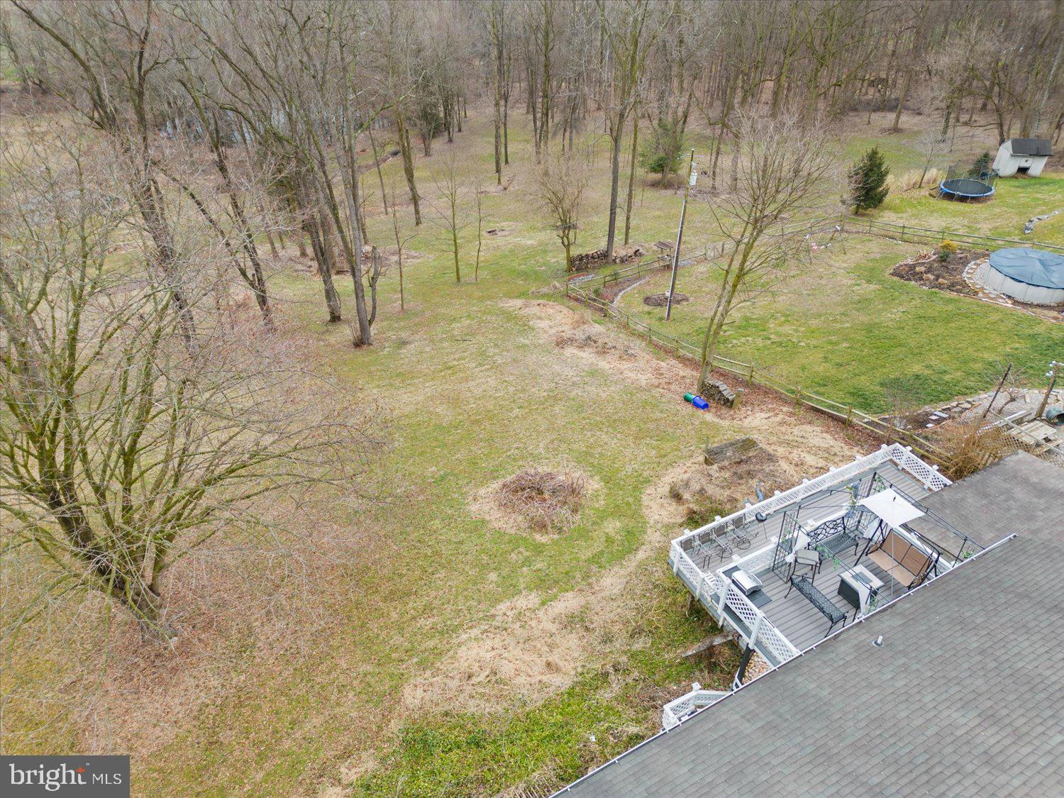 Aerial view of a wooded backyard with a broad lawn and furnished raised deck.
