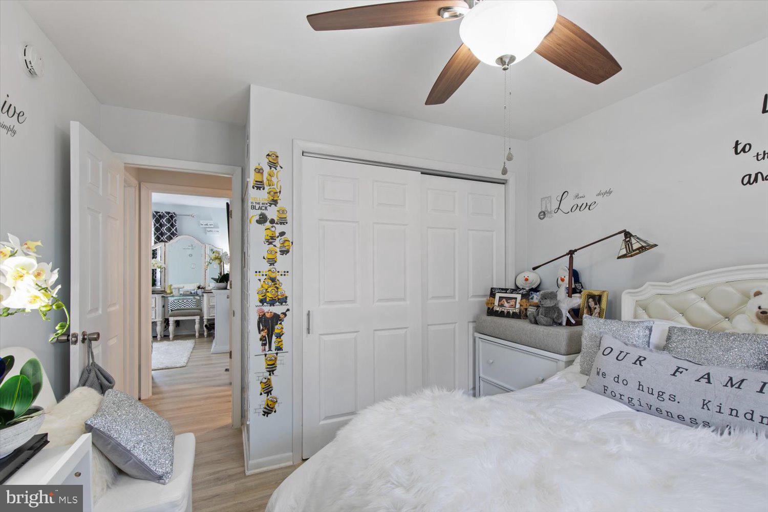 Bedroom with white bedding, sliding closet doors, Minions decals, and a wood-blade ceiling fan.