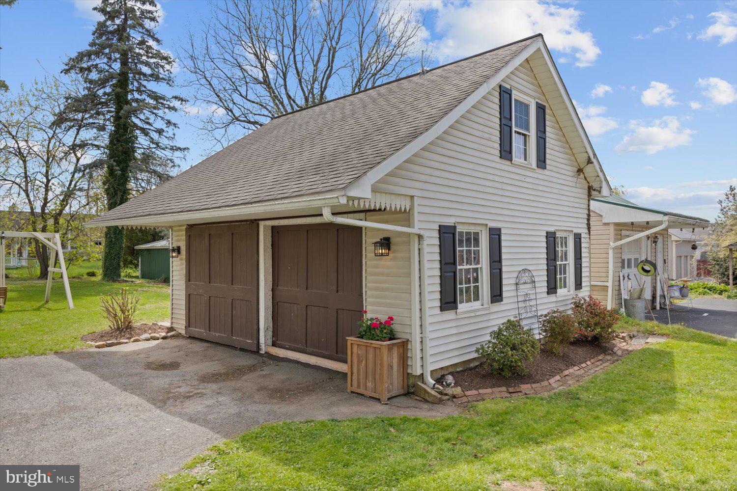Two-story cream garage with brown double doors, black shutters, and a steep shingled roof.