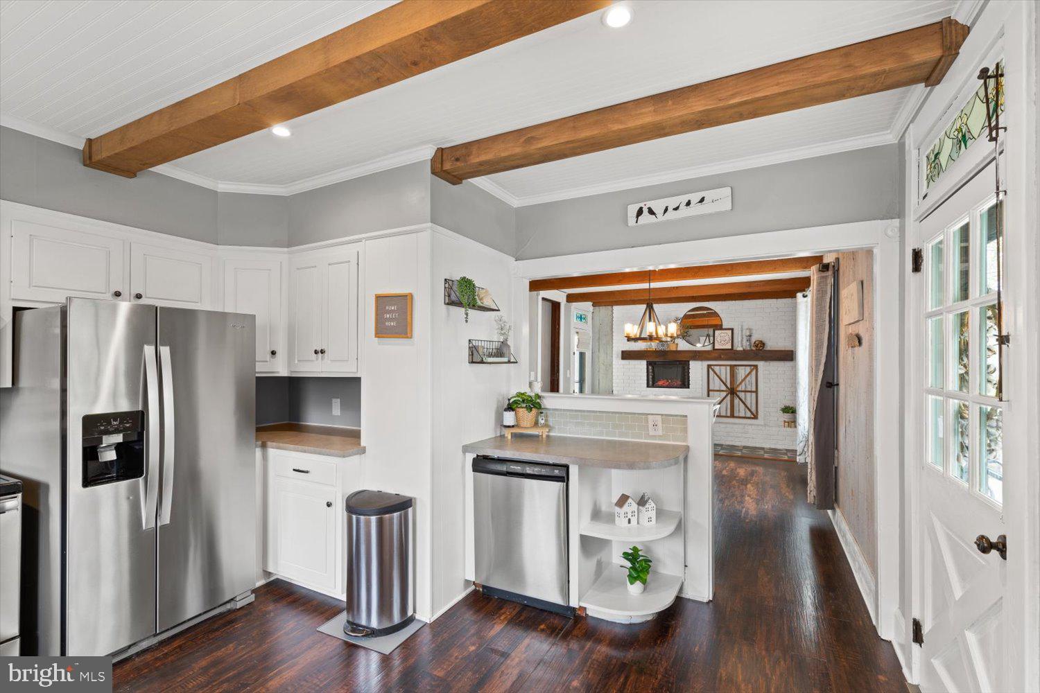 Kitchen with white cabinets, stainless steel appliances, exposed wood beams, and dark hardwood floors.