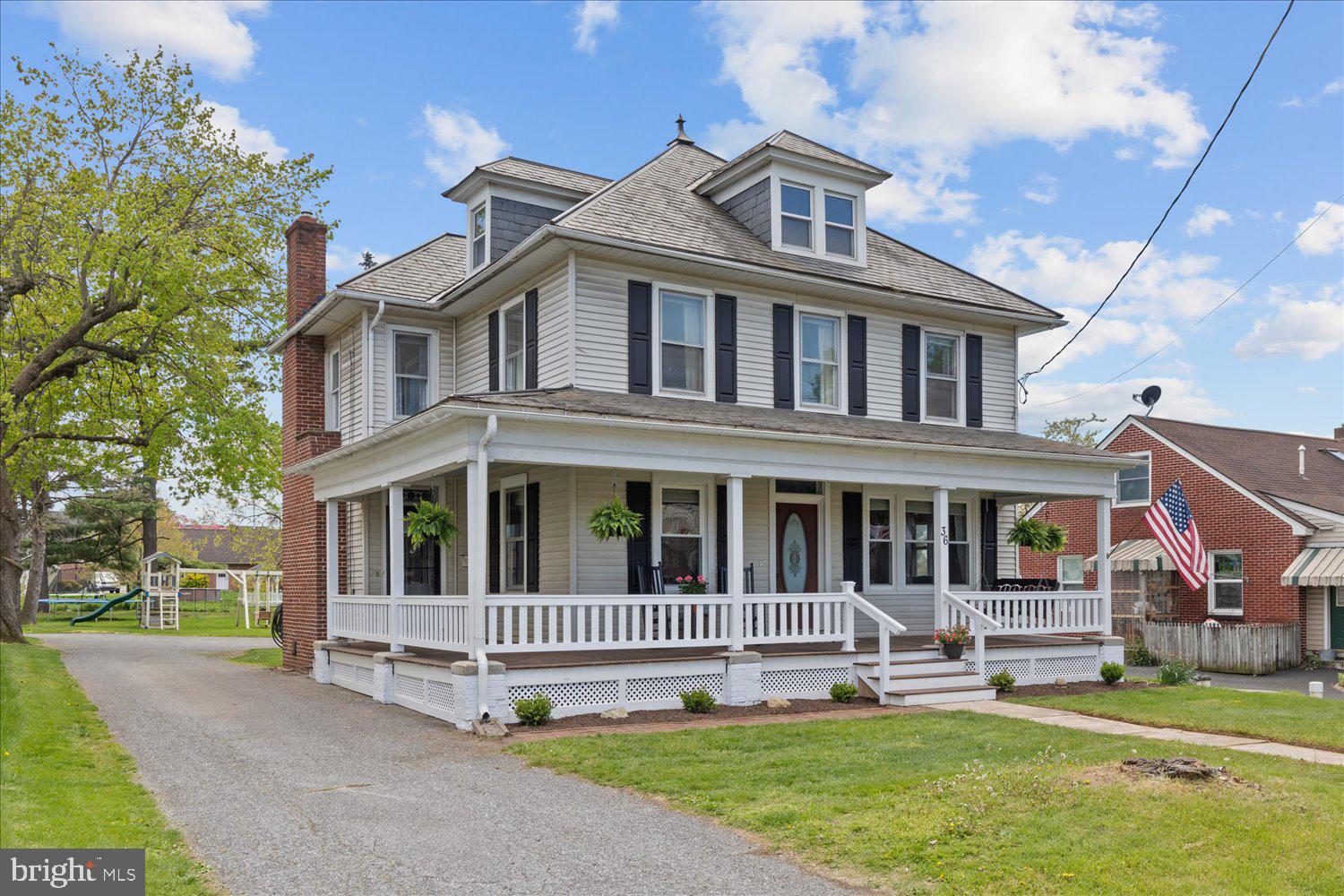 Two-story white house with black shutters, a broad wraparound porch, and gray shingle roof.