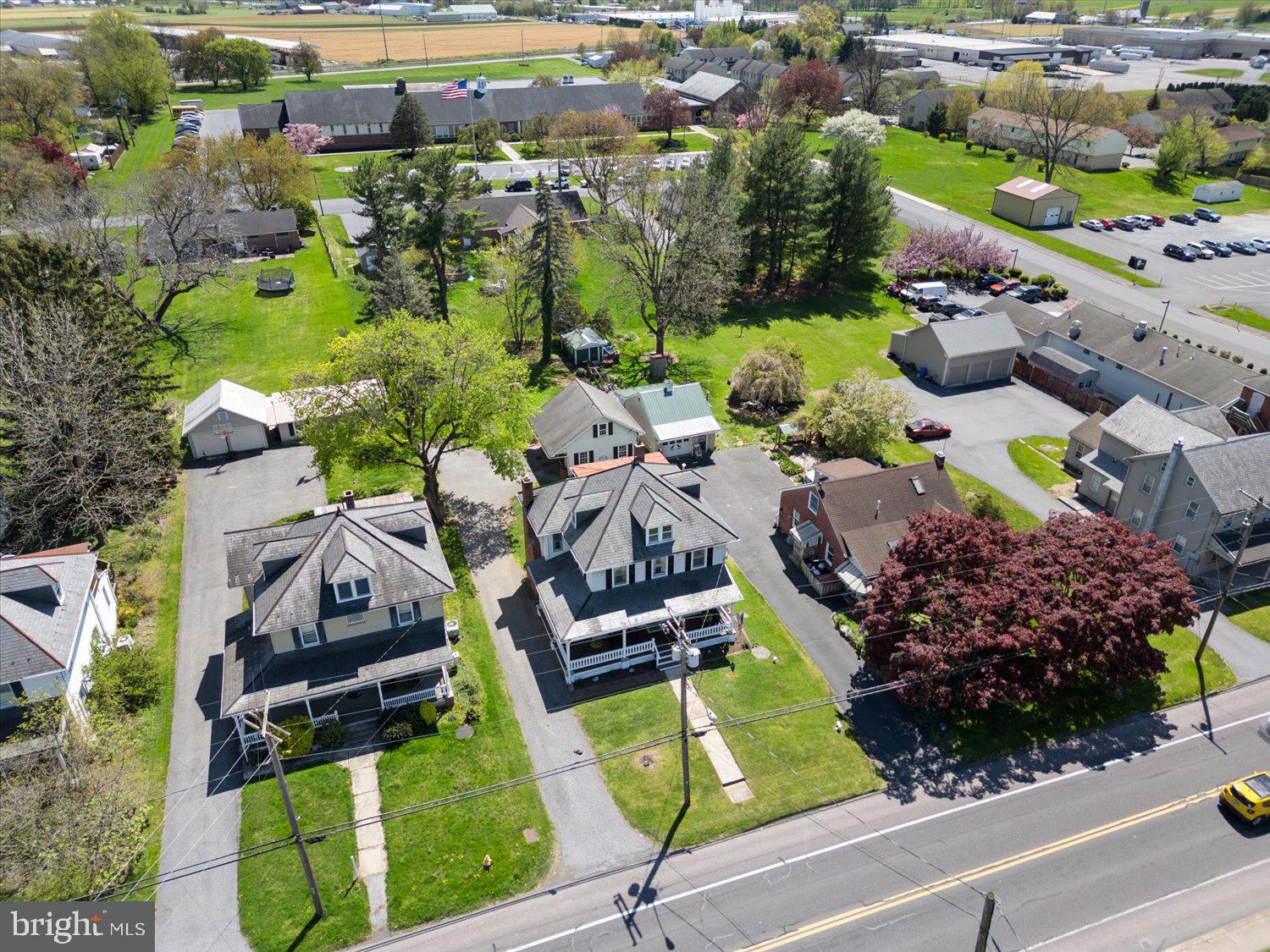 Aerial view of a detached house with a front porch, lawn, and driveway beside a main road.