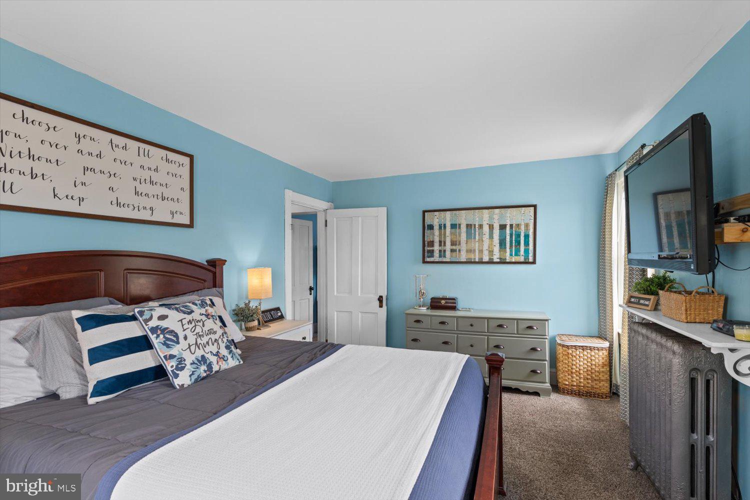 Blue bedroom with a dark wood bed, gray dresser, framed art, and television.