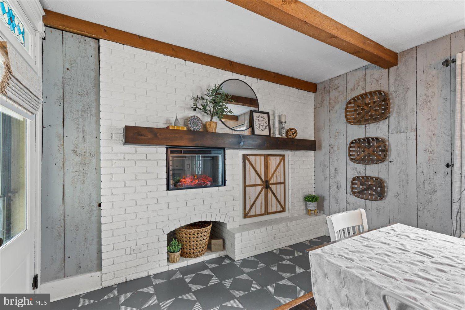 Dining room with a white brick fireplace, wood mantel, exposed beams, and patterned floor.