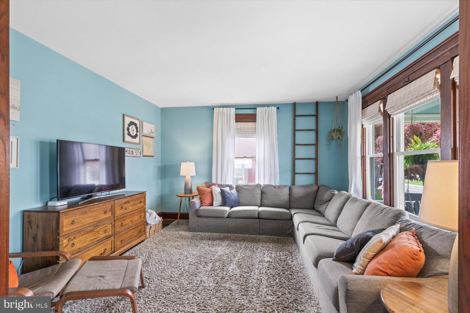 Living room with turquoise walls, a gray sectional sofa, and large wood-trimmed windows.