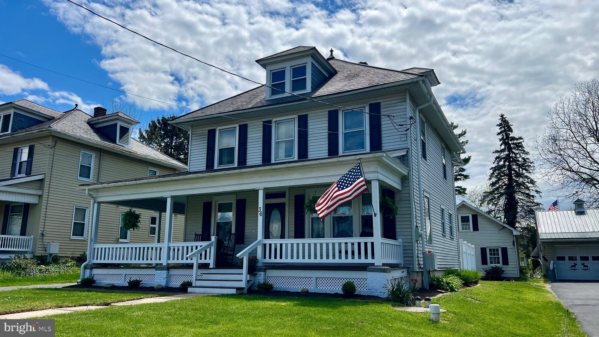 Two-story home with a covered porch, prominent dormer, dark shutters, and an American flag.