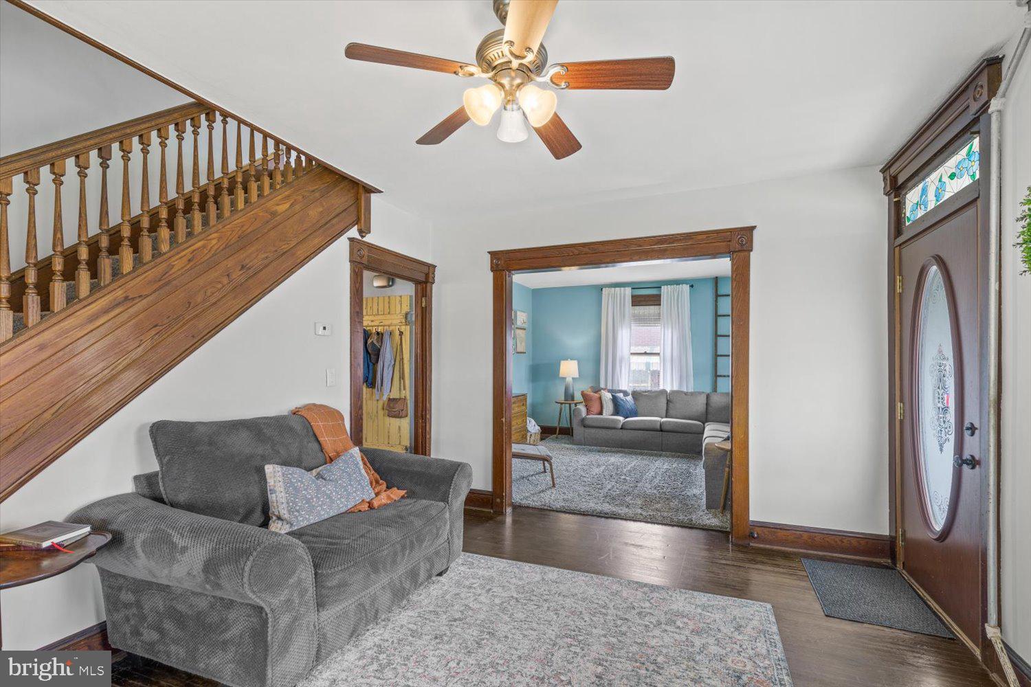 Living room and entry with a wooden staircase, stained-glass front door, and adjoining blue sitting room.