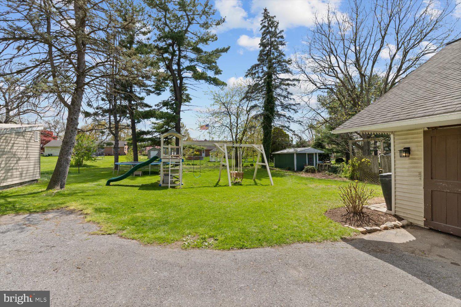 Backyard with a lawn, mature trees, and a children's playset with slide and swings.