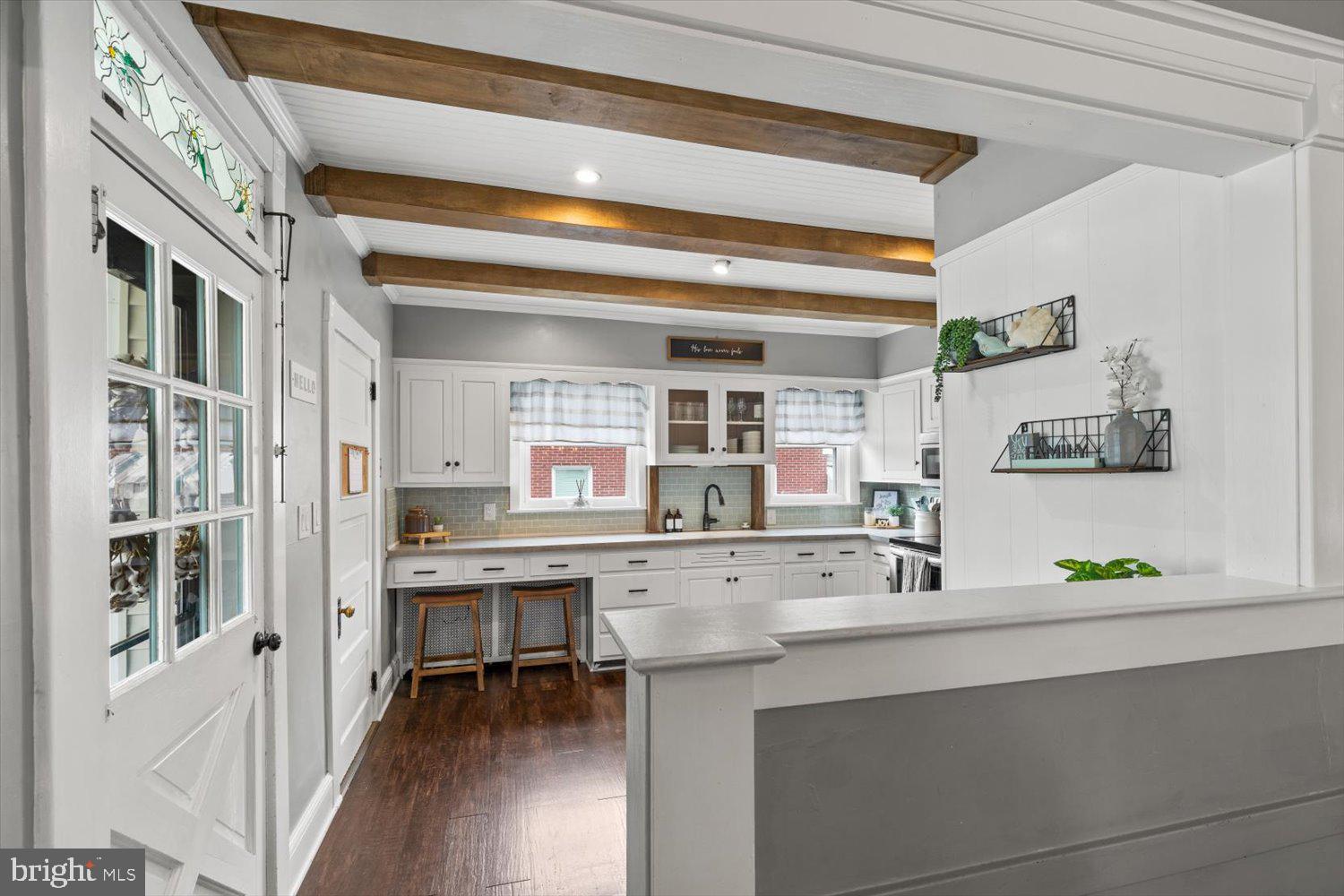 Kitchen with white cabinetry, exposed wood beams, and a large foreground counter.