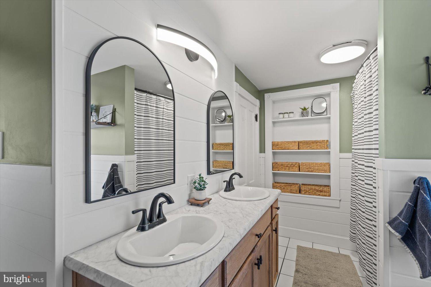 Bathroom with a double-sink vanity, arched mirrors, and built-in shelves with wicker baskets.